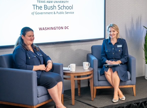 A photo of two women sitting on a stage during a presentation.