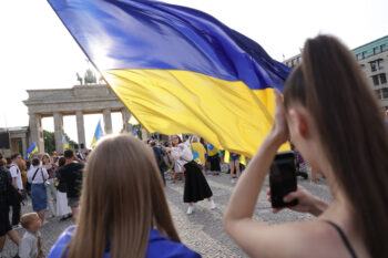 A woman waves a large Ukrainian flag in a crowd gathered in front of the Brandenburg Gate in Berlin