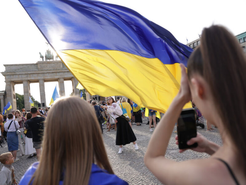Ukrainians gathered at the Brandenburg Gate watch on as a woman waves a large Ukrainian flag