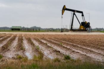 a photo of rainwater pooled between dirt rows in a field, with a black and yellow oil pump in the background