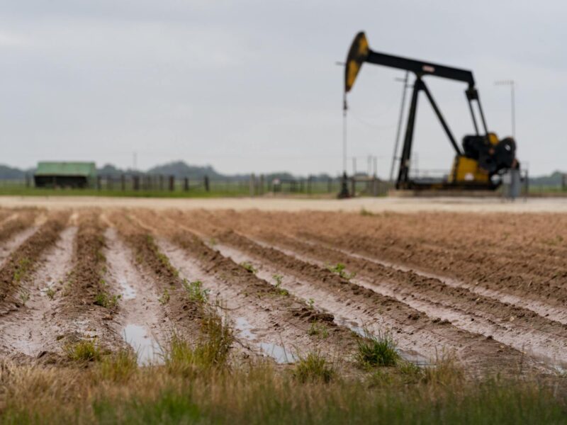 a photo of rainwater pooled between dirt rows in a field, with a black and yellow oil pump in the background