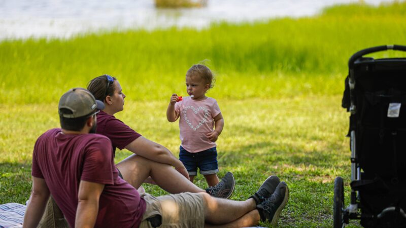 A photo of a young family on the grass near a lake.