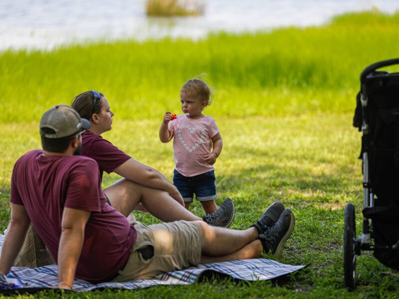 A photo of a young family on the grass near a lake.