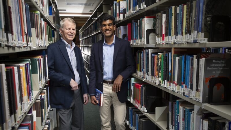 A photo of two men standing among shelves of books in a library.