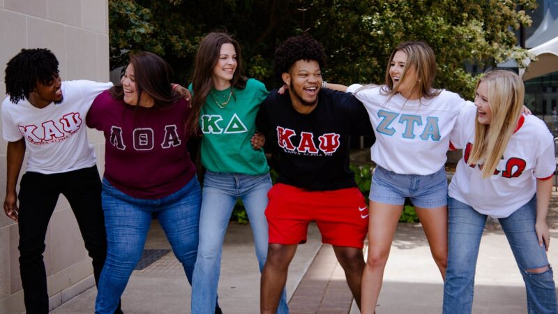six students wearing fraternity or sorority shirts sawin' em off