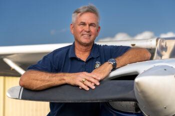 Close up of Russell McGee standing with arms resting on the propellor of a Cessna airplane.