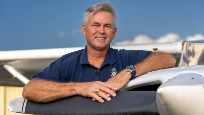 Close up of Russell McGee standing with arms resting on the propellor of a Cessna airplane.