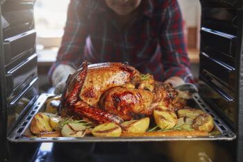 a stock photo of a woman removing a turkey surrounded by vegetables from an oven