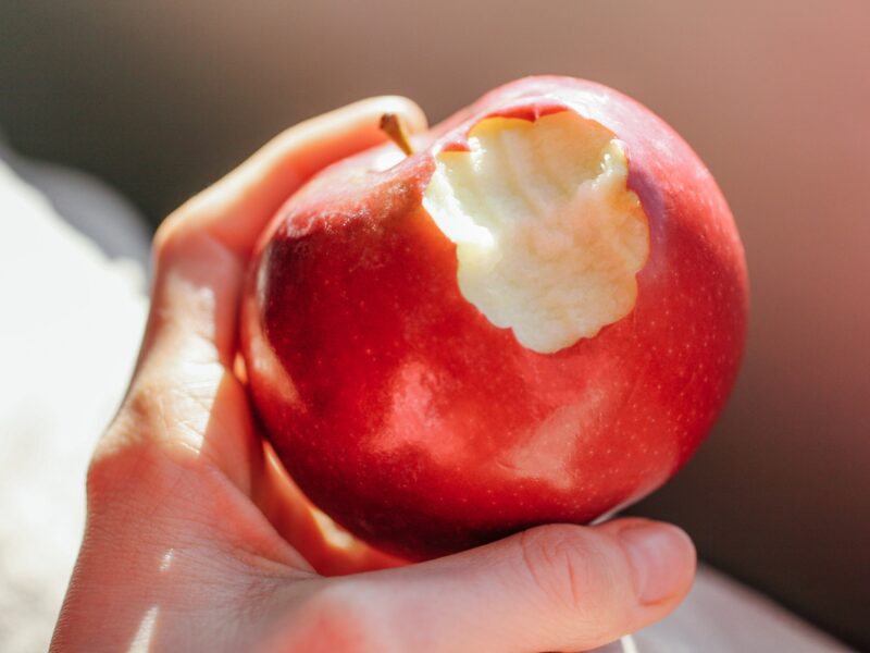 a hand holding a red apple with a bite taken out of it
