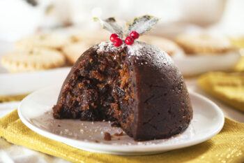 Christmas pudding with holly and mince pies in background and white and gold table colors