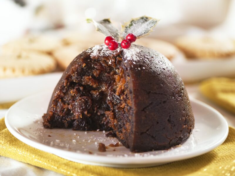 Christmas pudding with holly and mince pies in background and white and gold table colors