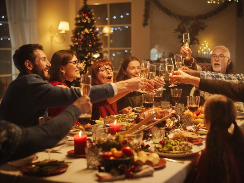 A photo of a family and friends at a Christmas dinner table celebrating a toast with raised glasses.