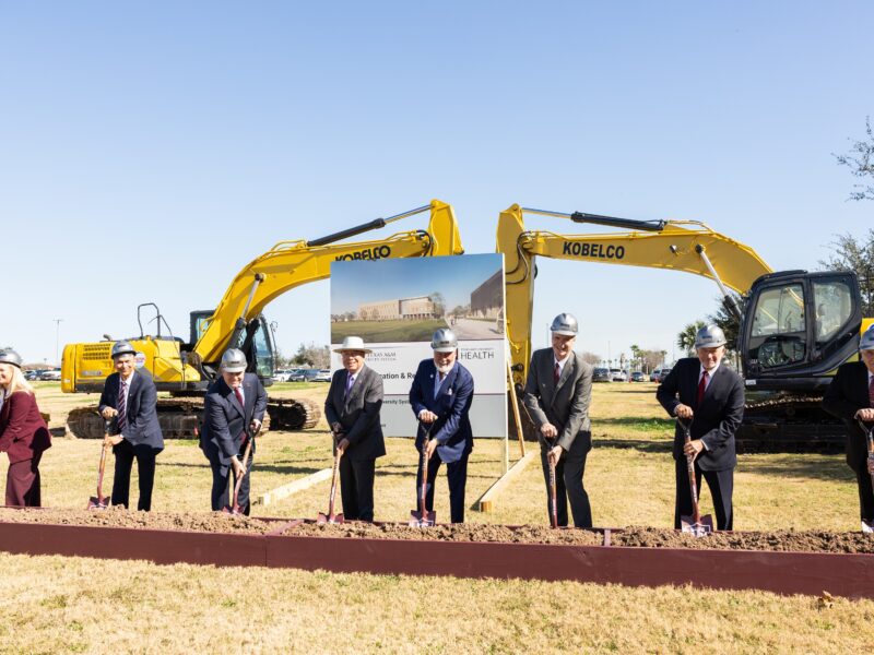 A photo of a group of people with shovels in front of heavy equipment for a groundbreaking ceremony.