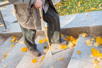 A photo of an elderly man using a cane as he climbs stairs in the fall.