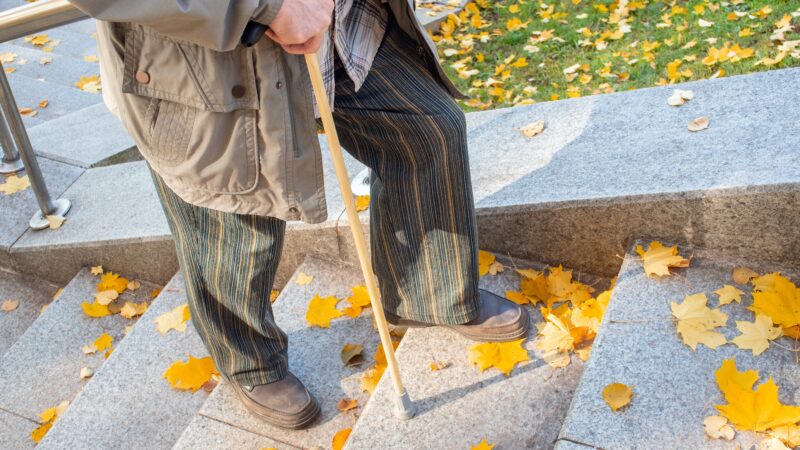 A photo of an elderly man using a cane as he climbs stairs in the fall.