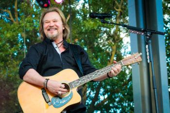 a photo of Travis Tritt smiling and strumming a guitar