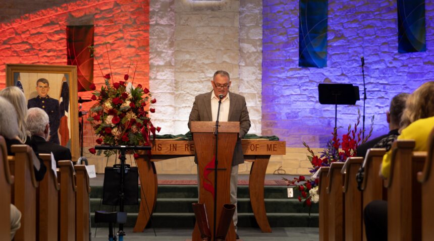 A photo of a man at a lectern in a church speaking during a memorial service.