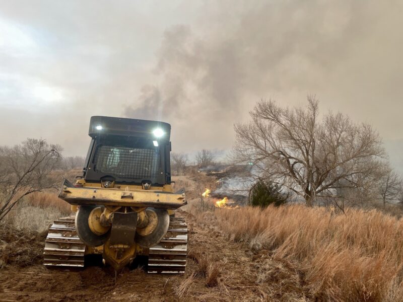 A fire burns in a field with a tractor sitting in the foreground