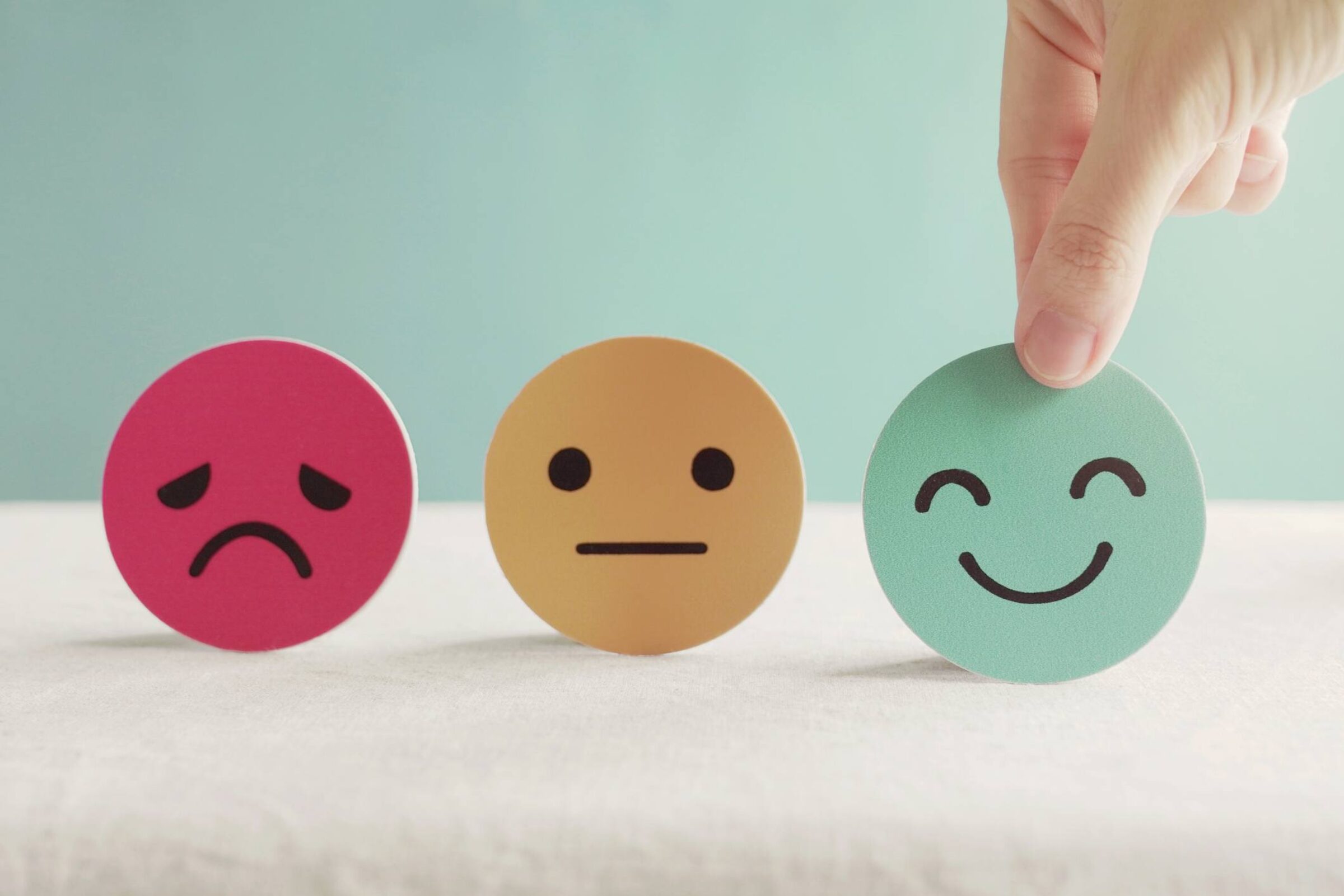 Cut outs of round faces depicting different emotions, with a hand selecting a smiling faces