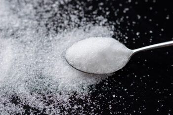 A spoon full of white sugar against a dark background