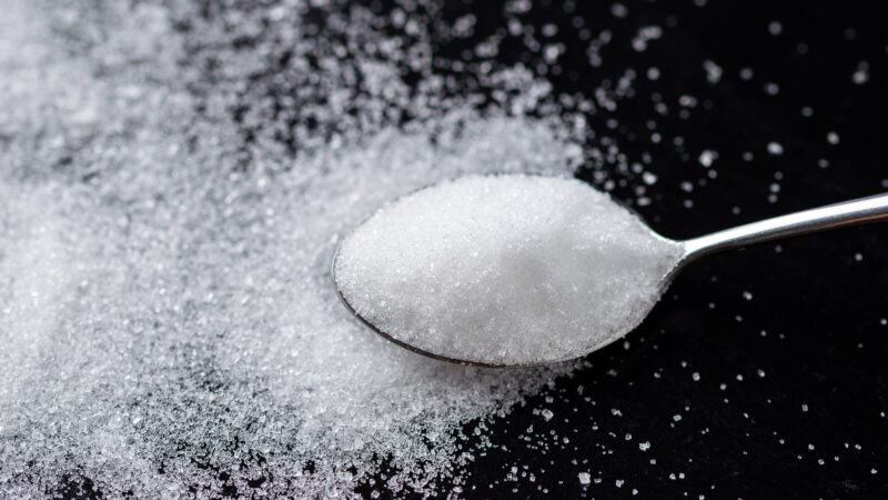 A spoon full of white sugar against a dark background