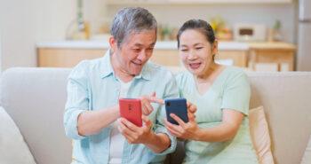 A photo of an Asian elderly couple asian elderly couple looking at their mobile phones together while sitting on a couch.