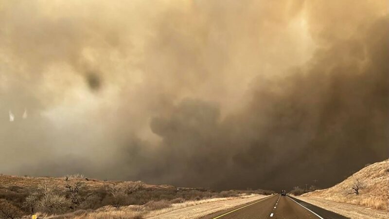 A photo of a highway with smoke from a wildfire blocking the sun in the background.