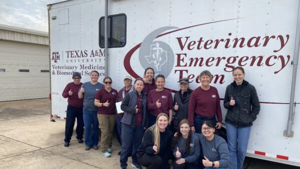A photo of a group of people standing in front of a trailer from the Texas A&M University Veterinary Emergency Team.