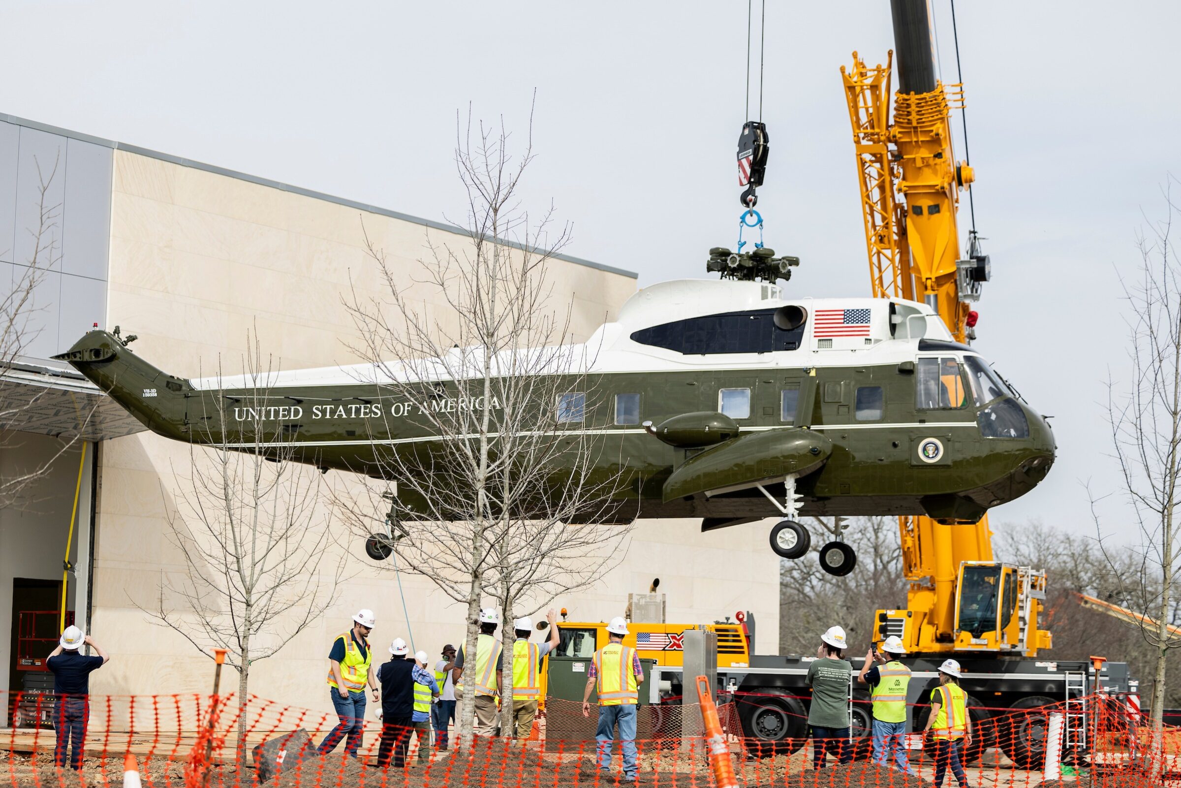 Marine One helicopter lifted by crane into the Pavilion building as construction workers look on