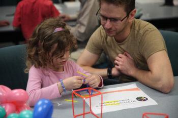 a child and her parent work on an activity at a previous fair event