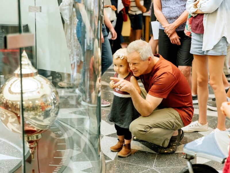 a man showing a toddler the pendulum in the Mitchell Physics Building foyer