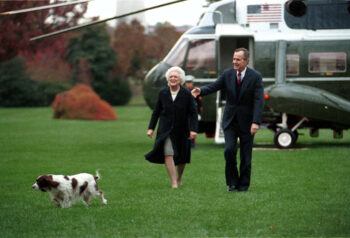 The president and first lady walk across the White House lawn with a helicopter in the background