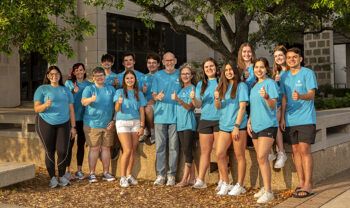 the group of students and a faculty member who went on the research trip, posing in matching shirts and giving the Gig 'em thumbs up on campus