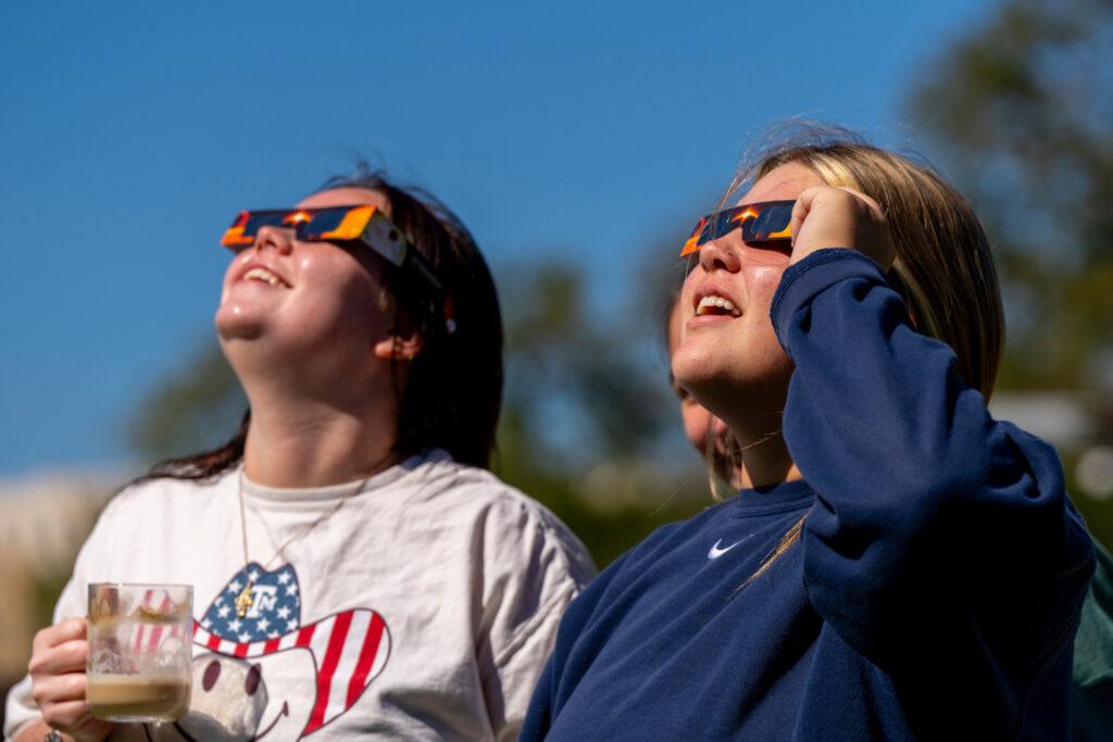Two women wearing eclipse glasses look up at the sky.