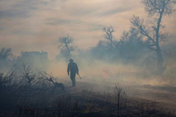a photo of a wildland firefighter walking down a dirt road surrounded by smoke