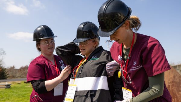 Two people wearing hard hats help a third person who is acting as a victim during a disaster training exercise.