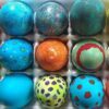 Overhead view of a carton of colorful dyed Easter eggs with a variety of designs.