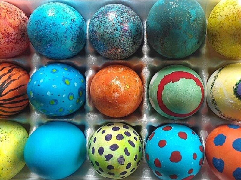 Overhead view of a carton of colorful dyed Easter eggs with a variety of designs.
