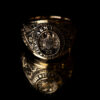 Close up photo of an Aggie Ring against a black background. The image of the ring is reflected on a glass surface.