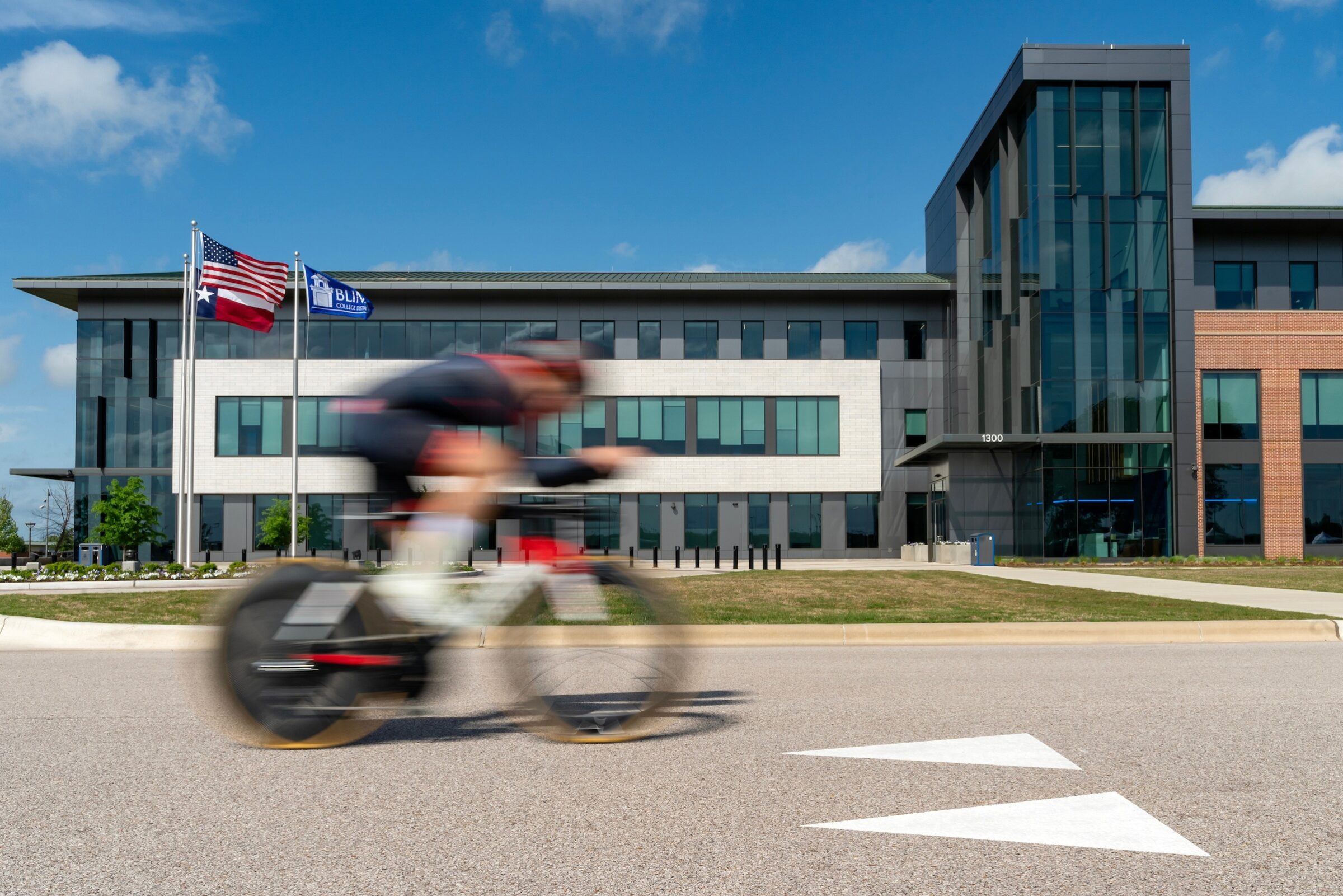 A bicyclist is blurred as they pedal past a building on the RELLIS Campus