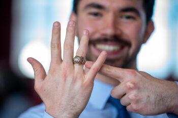 A young man smiles as he points to the Aggie Ring on his right hand.