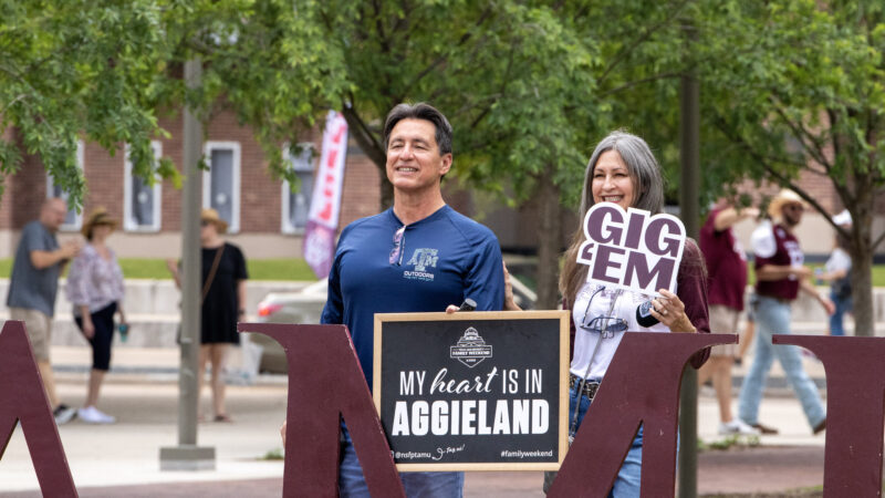 A man and a woman holding signs for a photo during Family Weekend on the Texas A&M campus.