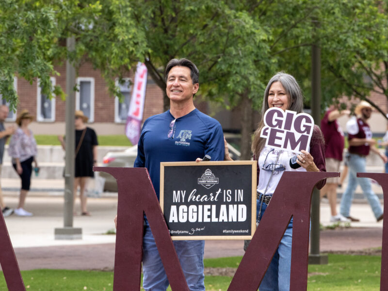 A man and a woman holding signs for a photo during Family Weekend on the Texas A&M campus.
