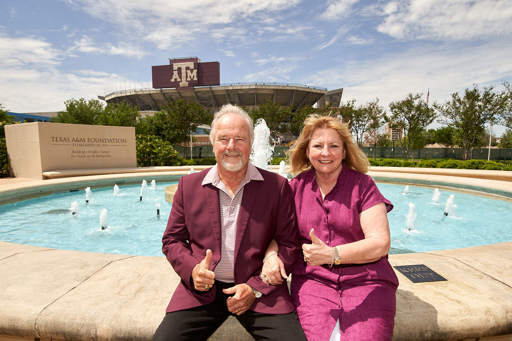 Pam and Larry Little posing for a portrait by a fountain at the Texas A&M Foundation with Kyle Field in the background.