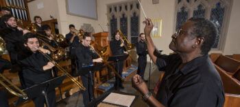 A conductor leading a trombone choir in a church.