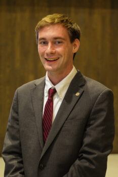 a photo of a young man in a suit and tie smiling indoors