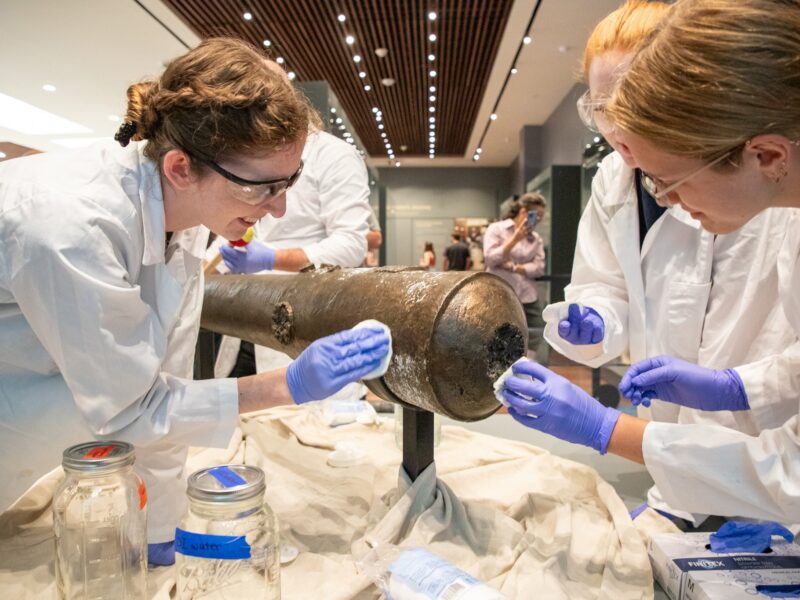 Nautical Archaeology Program graduate students Kimberly Breyfogle '23 (left), Alyssa Carpenter '22 (center) and Marissa Agerton '25 (right) gently clean the exterior of a four-pound bronze cannon used in the Battle of the Alamo.