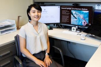 A photo of a researcher sitting at a desk with a computer monitor behind her.