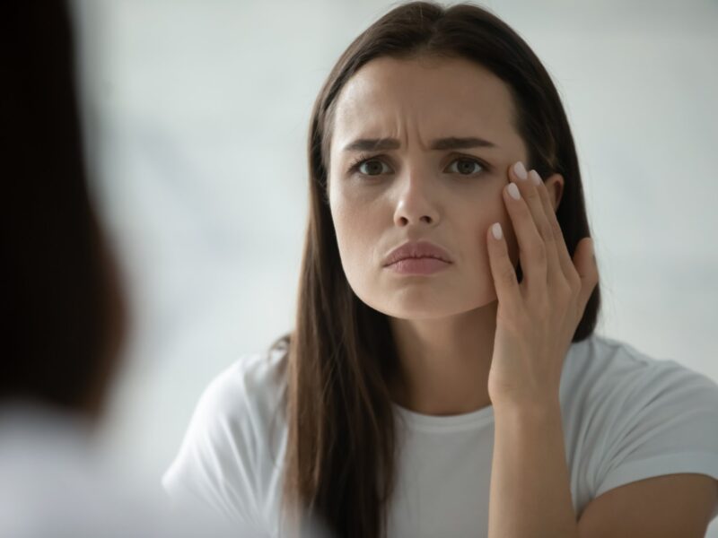 Close up head shot of an unhappy young woman checking skin