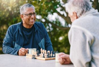 Chess, nature and retirement with senior friends playing a boardgame while bonding outdoor during summer.